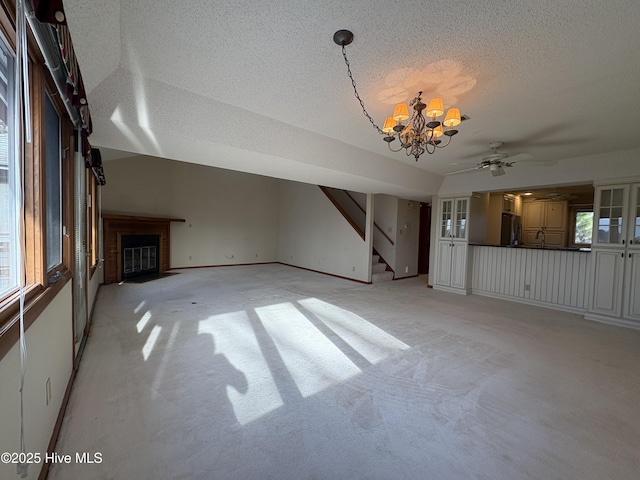 unfurnished living room featuring ceiling fan with notable chandelier, light colored carpet, and lofted ceiling