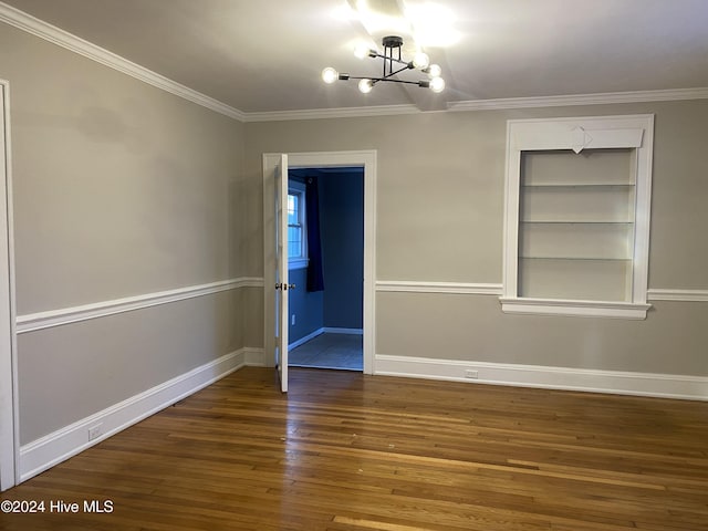 spare room with a chandelier, built in features, wood-type flooring, and ornamental molding