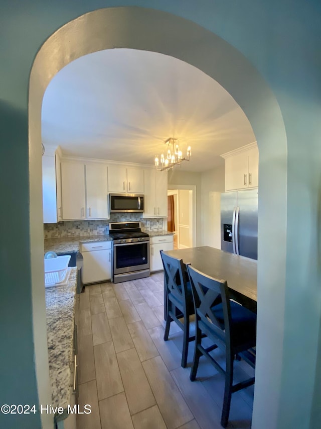 1121 Vance St N, Wilson, NC 27893 - kitchen with appliances with stainless steel finishes, a chandelier, white cabinetry, backsplash, and light wood-style floors