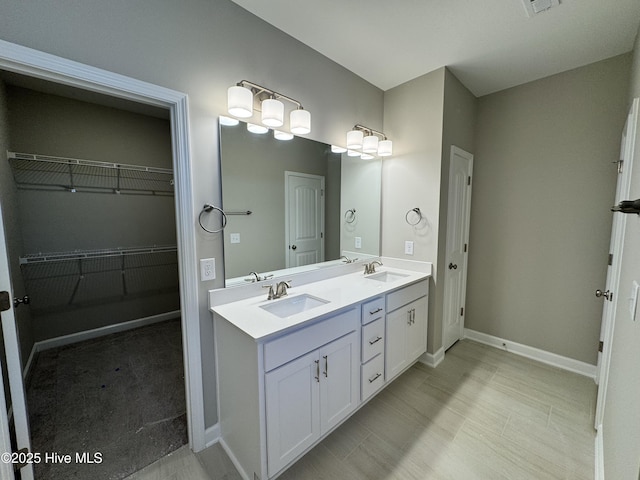 full bathroom with a sink, double vanity, a walk in closet, and baseboards