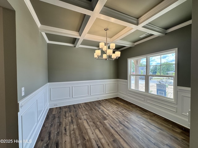 unfurnished dining area with coffered ceiling, dark wood-style flooring, an inviting chandelier, a wainscoted wall, and beam ceiling