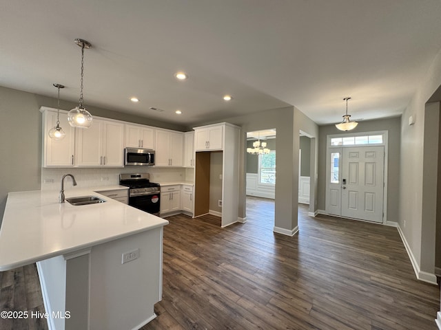 kitchen featuring dark wood finished floors, a sink, a peninsula, white cabinets, and appliances with stainless steel finishes