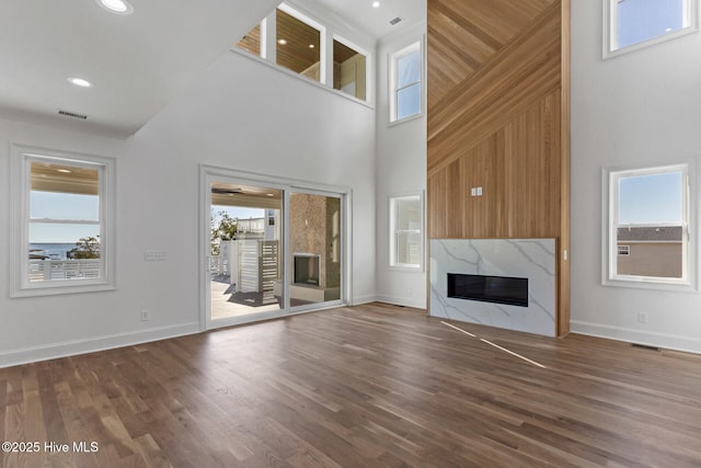 unfurnished living room with hardwood / wood-style floors, a towering ceiling, and a premium fireplace