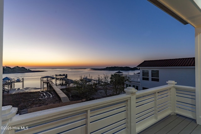 balcony at dusk featuring a water view and a dock