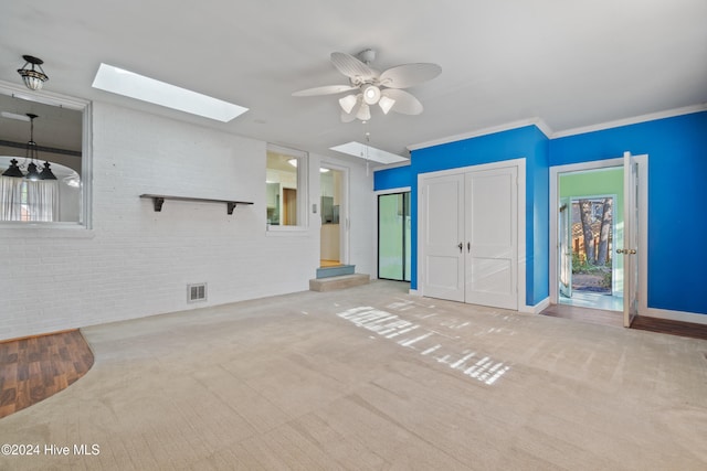 unfurnished living room with light carpet, a skylight, ornamental molding, brick wall, and ceiling fan