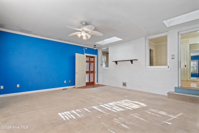 unfurnished room with carpet flooring, a skylight, ceiling fan, and brick wall