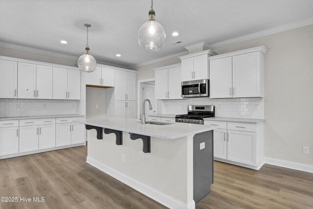 2786 Longleaf Pine Cir, Leland, NC 28451 - kitchen with stainless steel appliances, ornamental molding, a center island with sink, light wood-style floors, and light countertops