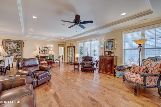 living room featuring ceiling fan with notable chandelier, light wood-type flooring, a tray ceiling, and ornamental molding