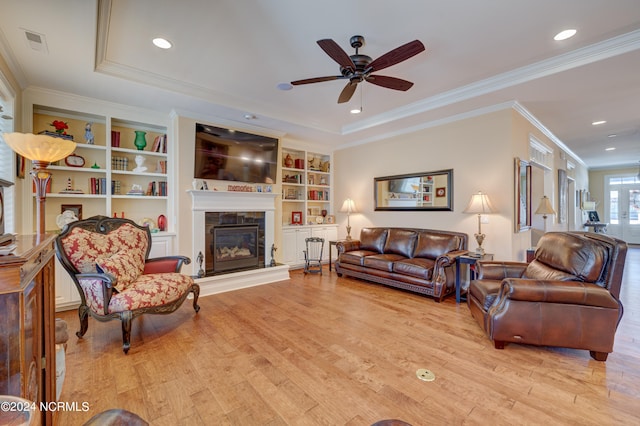 living room with built in shelves, light wood-type flooring, ceiling fan, and ornamental molding