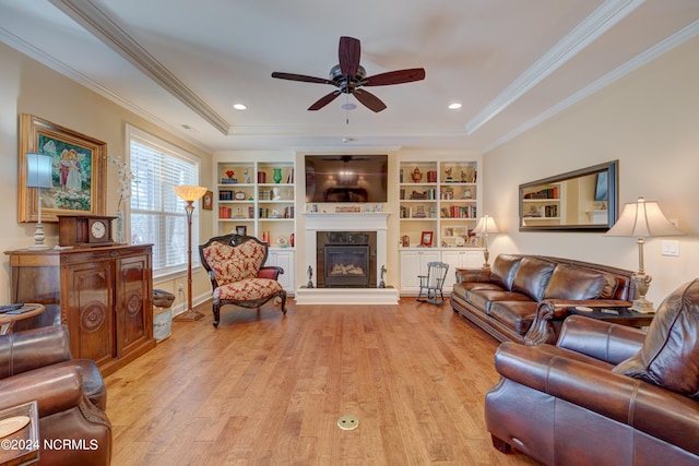 living room featuring ceiling fan, light wood-type flooring, ornamental molding, and a tray ceiling