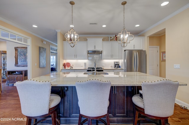 kitchen featuring stainless steel refrigerator, a large island with sink, a breakfast bar area, white cabinets, and ornamental molding