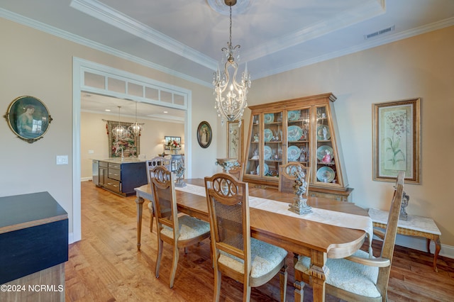 dining space featuring a notable chandelier, light hardwood / wood-style floors, a raised ceiling, and ornamental molding