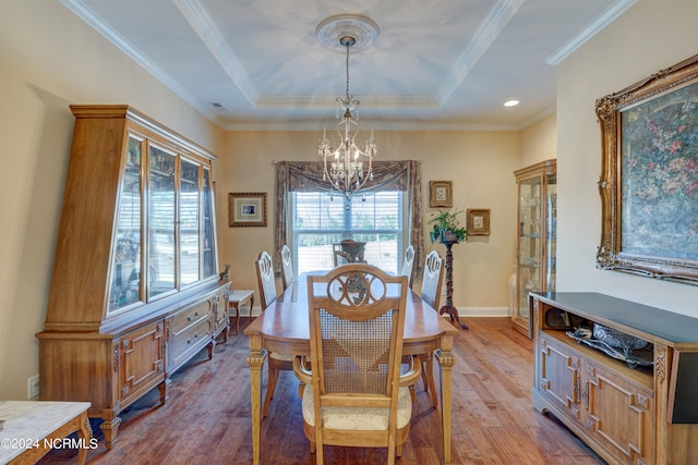 dining space with an inviting chandelier, light wood-type flooring, ornamental molding, and a tray ceiling