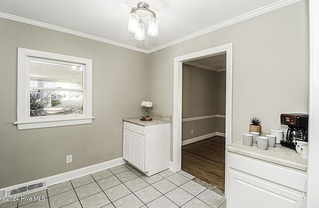 interior space featuring light tile patterned floors, a textured ceiling, ornamental molding, and white cabinets