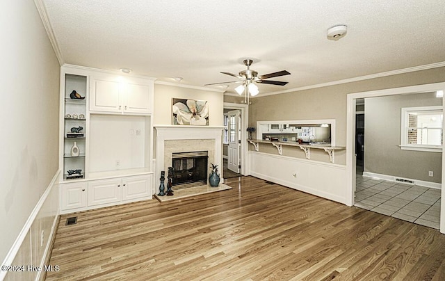 unfurnished living room with hardwood / wood-style flooring, ornamental molding, ceiling fan, a high end fireplace, and a textured ceiling