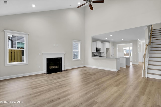 unfurnished living room featuring a wealth of natural light, light hardwood / wood-style flooring, high vaulted ceiling, and ceiling fan