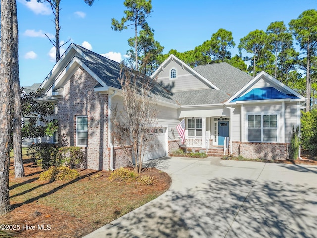 craftsman inspired home featuring a shingled roof, concrete driveway, an attached garage, covered porch, and brick siding