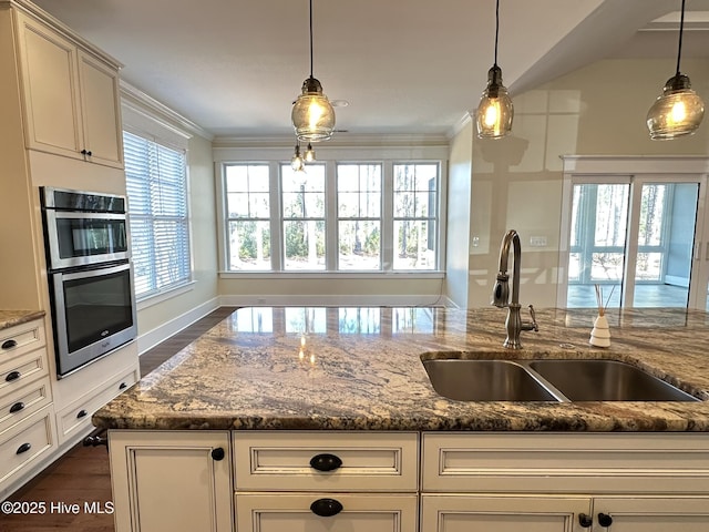 kitchen with stainless steel double oven, dark stone countertops, a sink, and pendant lighting