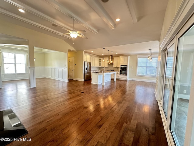 unfurnished living room with vaulted ceiling with beams, a decorative wall, dark wood-type flooring, wainscoting, and ceiling fan