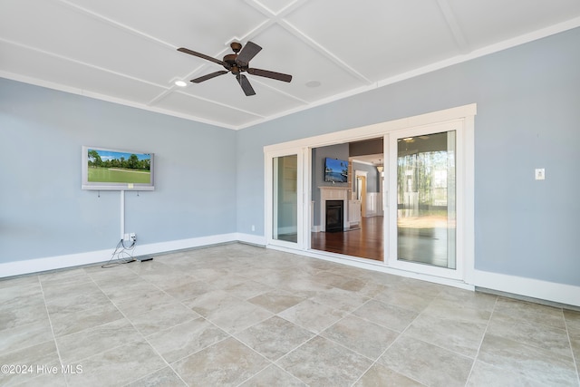 empty room with a ceiling fan, a glass covered fireplace, coffered ceiling, and baseboards