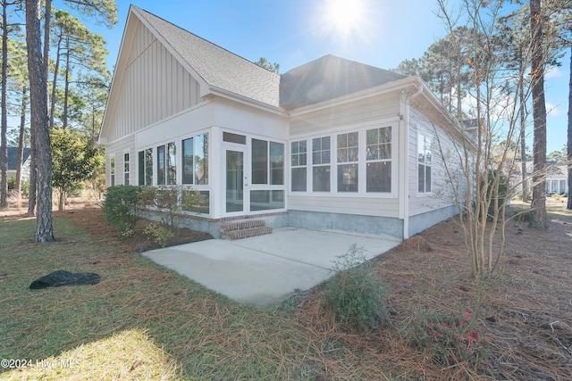 rear view of house with a shingled roof, a sunroom, a patio, and a lawn