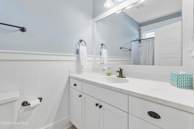 bathroom featuring curtained shower, visible vents, toilet, wainscoting, and vanity