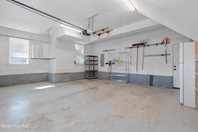 garage featuring electric panel, a garage door opener, and freestanding refrigerator