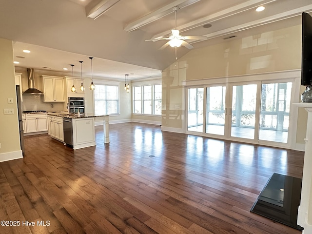 unfurnished living room with ceiling fan, lofted ceiling with beams, a sink, baseboards, and dark wood finished floors