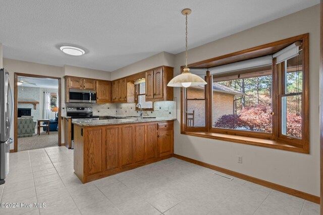 kitchen featuring a large fireplace, hanging light fixtures, stainless steel appliances, kitchen peninsula, and decorative backsplash