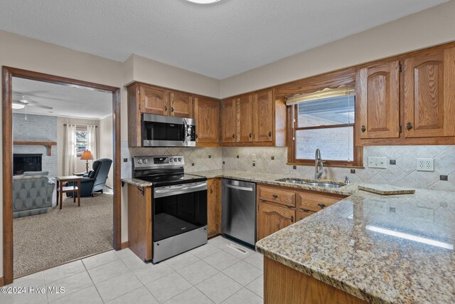 kitchen featuring appliances with stainless steel finishes, light stone counters, light colored carpet, ceiling fan, and sink