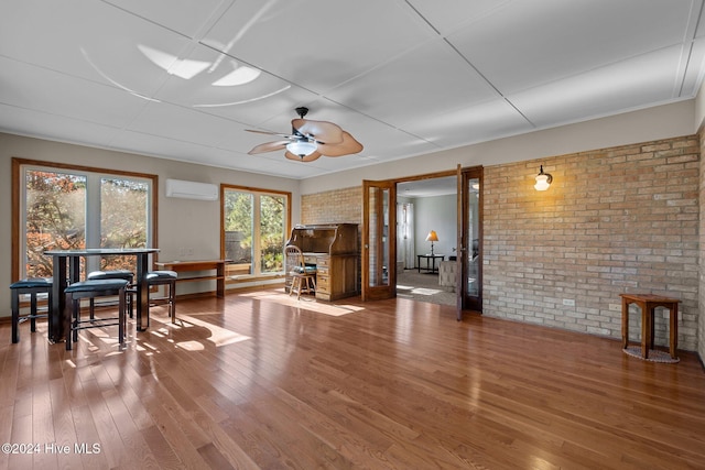 miscellaneous room featuring ceiling fan, brick wall, wood-type flooring, and a wall unit AC