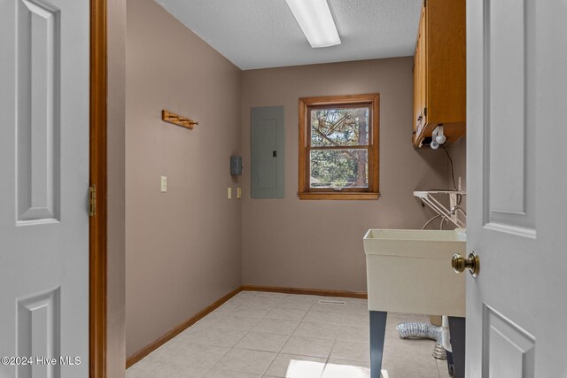 clothes washing area featuring electric panel, light tile patterned floors, cabinets, and a textured ceiling