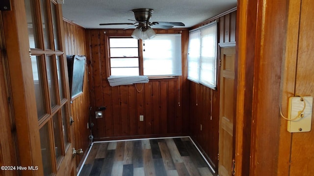 interior space featuring wood walls, ceiling fan, dark wood-type flooring, and a textured ceiling