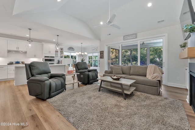 living room with ceiling fan with notable chandelier, light wood-type flooring, and high vaulted ceiling