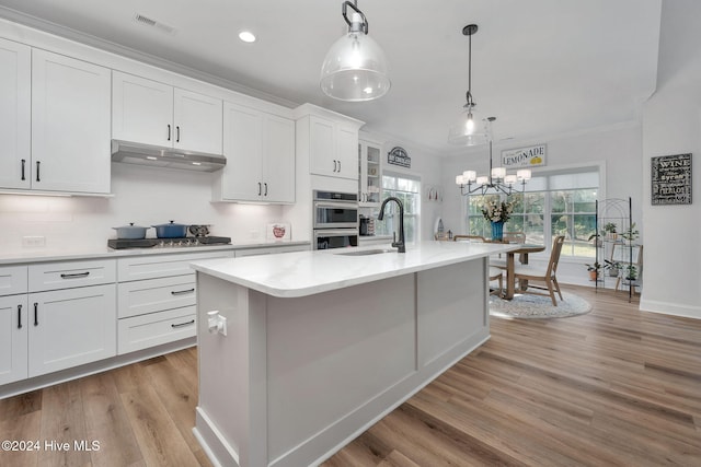 kitchen with pendant lighting, a center island with sink, sink, light wood-type flooring, and white cabinetry