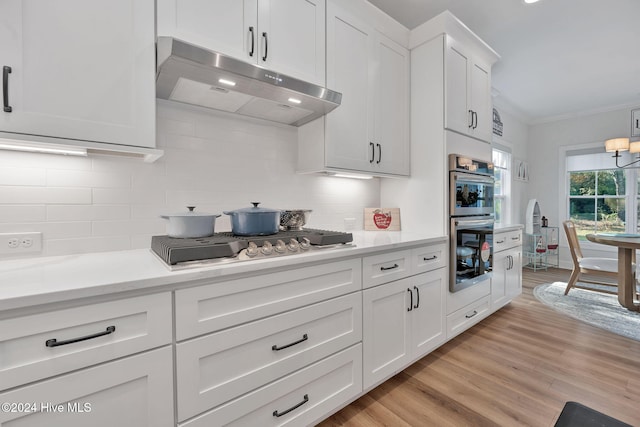 kitchen with backsplash, white cabinets, crown molding, light hardwood / wood-style floors, and stainless steel appliances