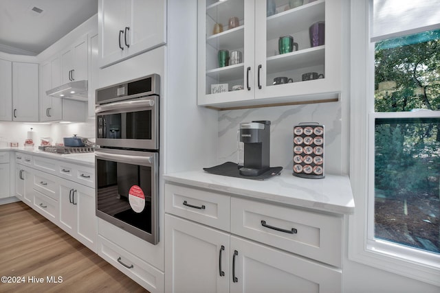 kitchen with white cabinetry, stainless steel appliances, light stone counters, light hardwood / wood-style floors, and decorative backsplash