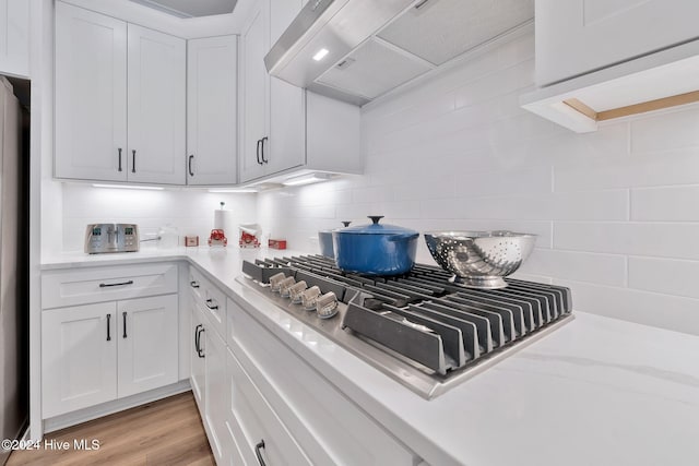 kitchen with exhaust hood, light wood-type flooring, tasteful backsplash, white cabinetry, and stainless steel gas cooktop