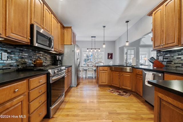 kitchen featuring sink, light hardwood / wood-style flooring, backsplash, decorative light fixtures, and appliances with stainless steel finishes