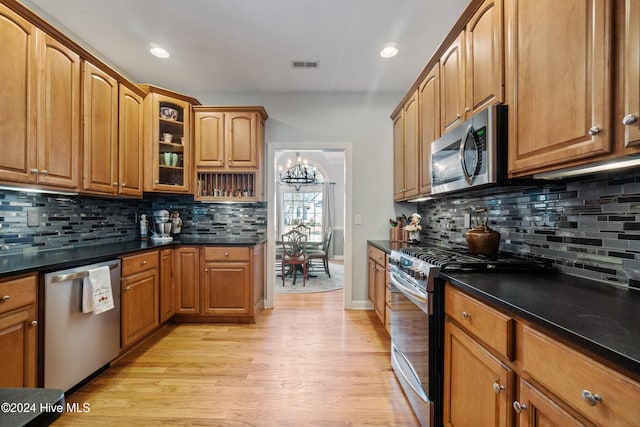 kitchen featuring tasteful backsplash, dark stone countertops, a chandelier, light hardwood / wood-style floors, and appliances with stainless steel finishes