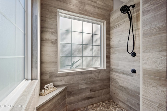 bathroom with a tile shower and wood walls