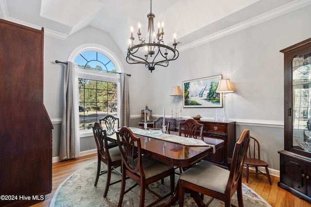 dining area with a notable chandelier, ornamental molding, lofted ceiling, and light wood-type flooring