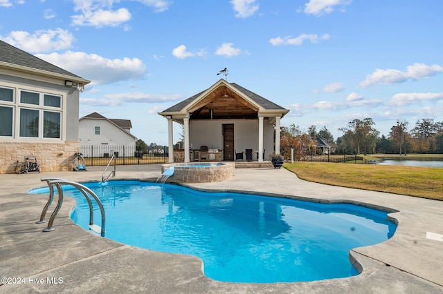 view of swimming pool with a lawn, a water view, pool water feature, a patio area, and exterior fireplace