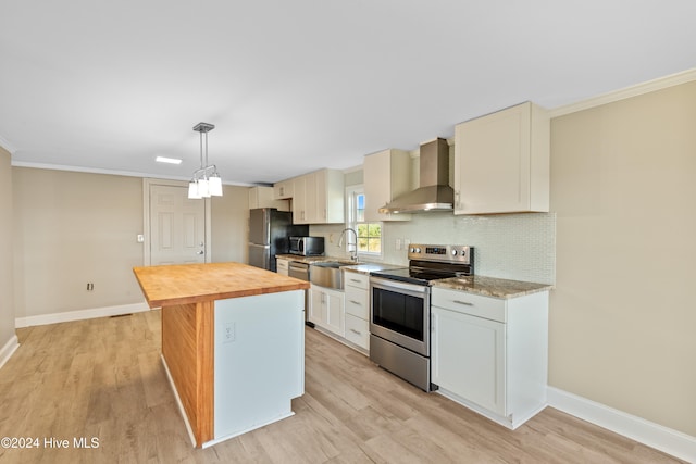 kitchen featuring a center island, wall chimney range hood, butcher block countertops, pendant lighting, and appliances with stainless steel finishes