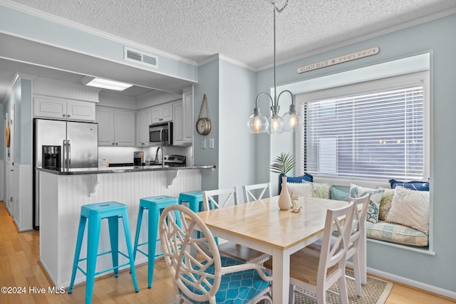 dining room featuring sink, ornamental molding, a textured ceiling, and light hardwood / wood-style flooring