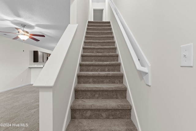 staircase featuring carpet, ceiling fan, lofted ceiling, and a textured ceiling