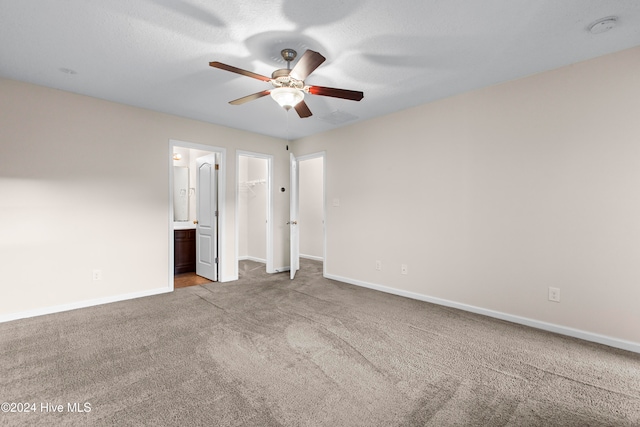 unfurnished bedroom featuring light carpet, ensuite bathroom, ceiling fan, a spacious closet, and a closet