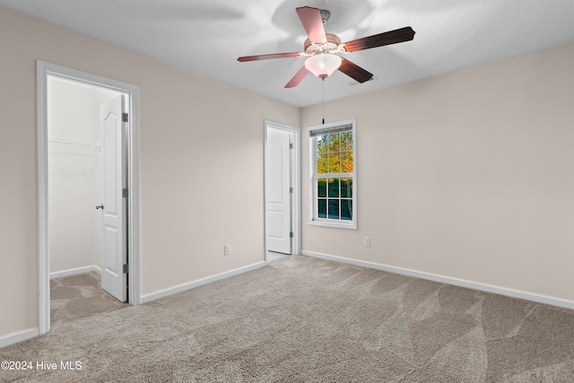 unfurnished bedroom featuring a walk in closet, a textured ceiling, light colored carpet, ceiling fan, and a closet