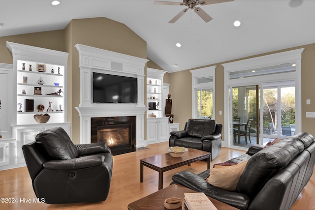 living room featuring light wood-type flooring, built in shelves, a large fireplace, vaulted ceiling, and ceiling fan