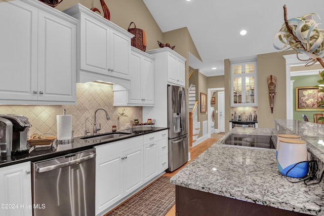 kitchen with dark stone counters, white cabinets, sink, vaulted ceiling, and appliances with stainless steel finishes